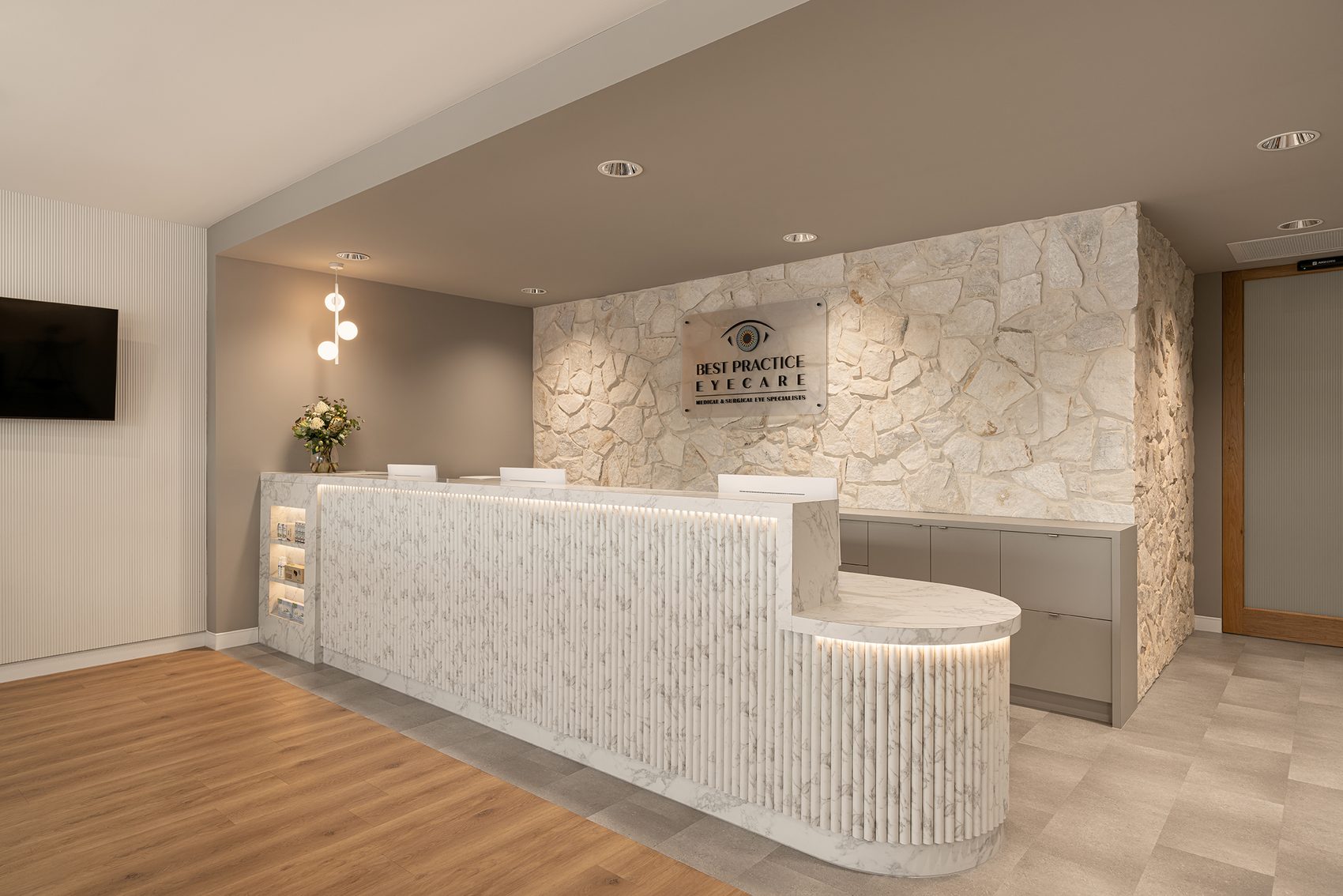 Long reception counter clad in ribbed stone, below signage on a stone feature wall, with a timber floor