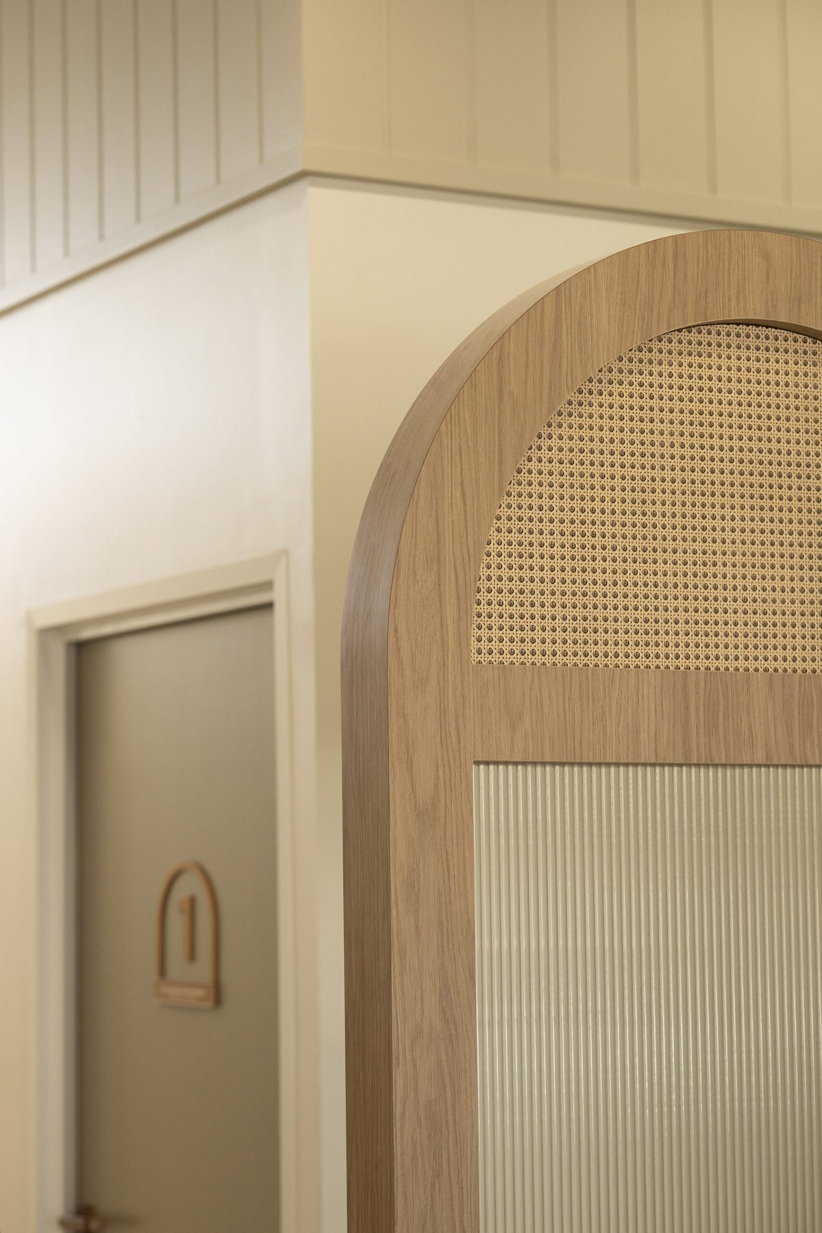 Curved timber battened archway beside a door in a white lined corridor, lit by a pendant